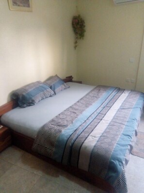 A bedroom with a bed, pillows, a nightstand, a wall-mounted plant, and a light switch.