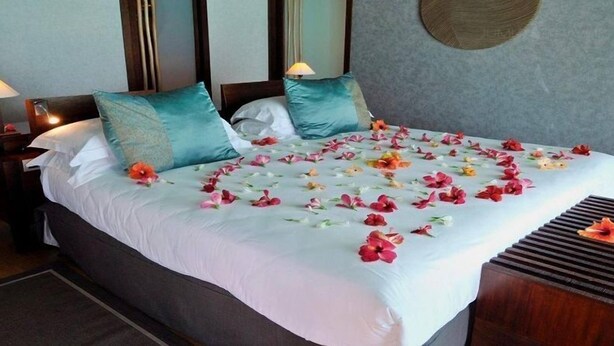 Un llit ben arropat amb estovatge blanc, almoiners color cel i un arranjament floral sobre el llit.