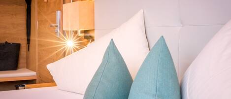 A bed with white and teal pillows, a wooden wall, and a lamp.