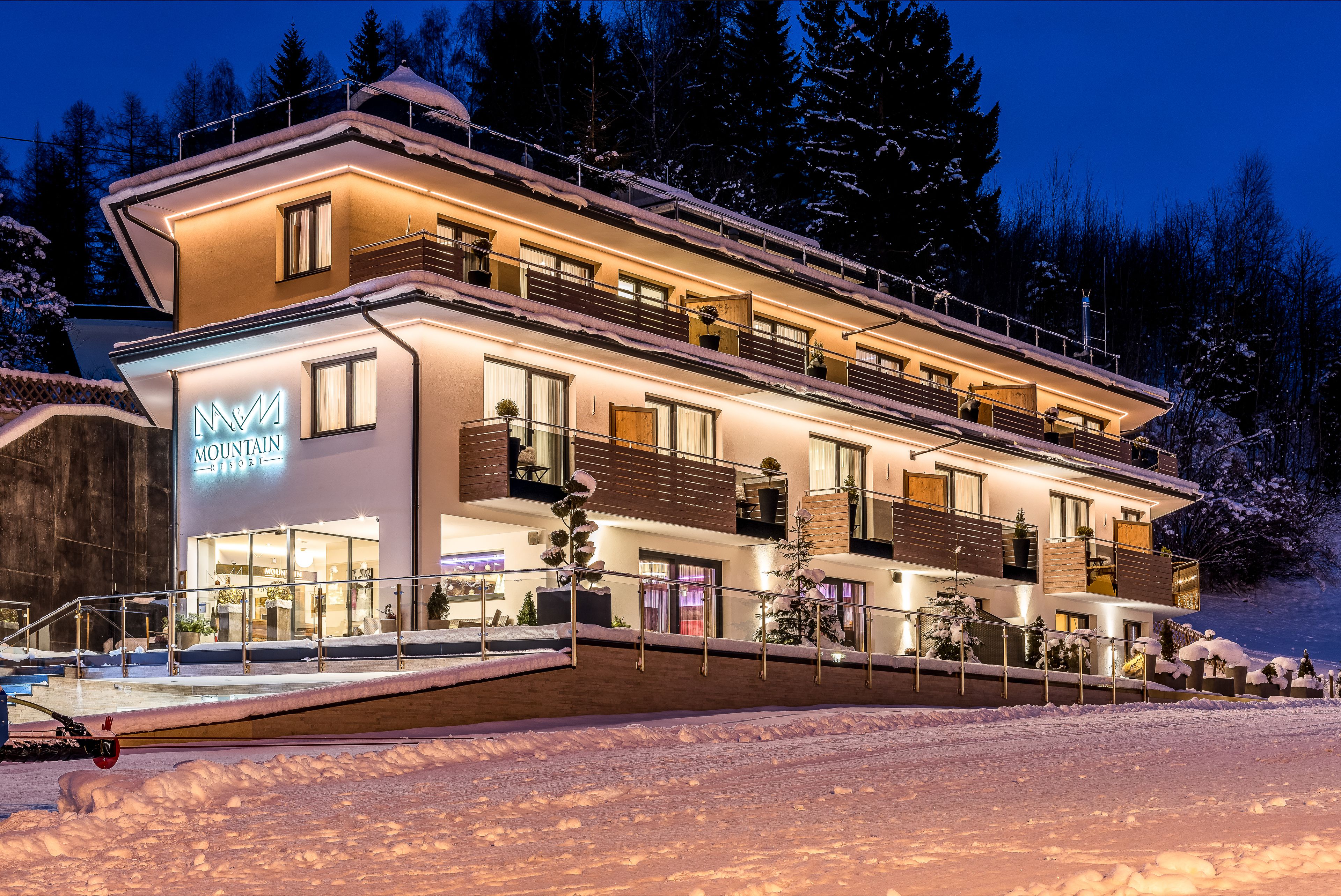 A multi-story hotel with a ski resort sign, balconies, and a snow-covered landscape.
