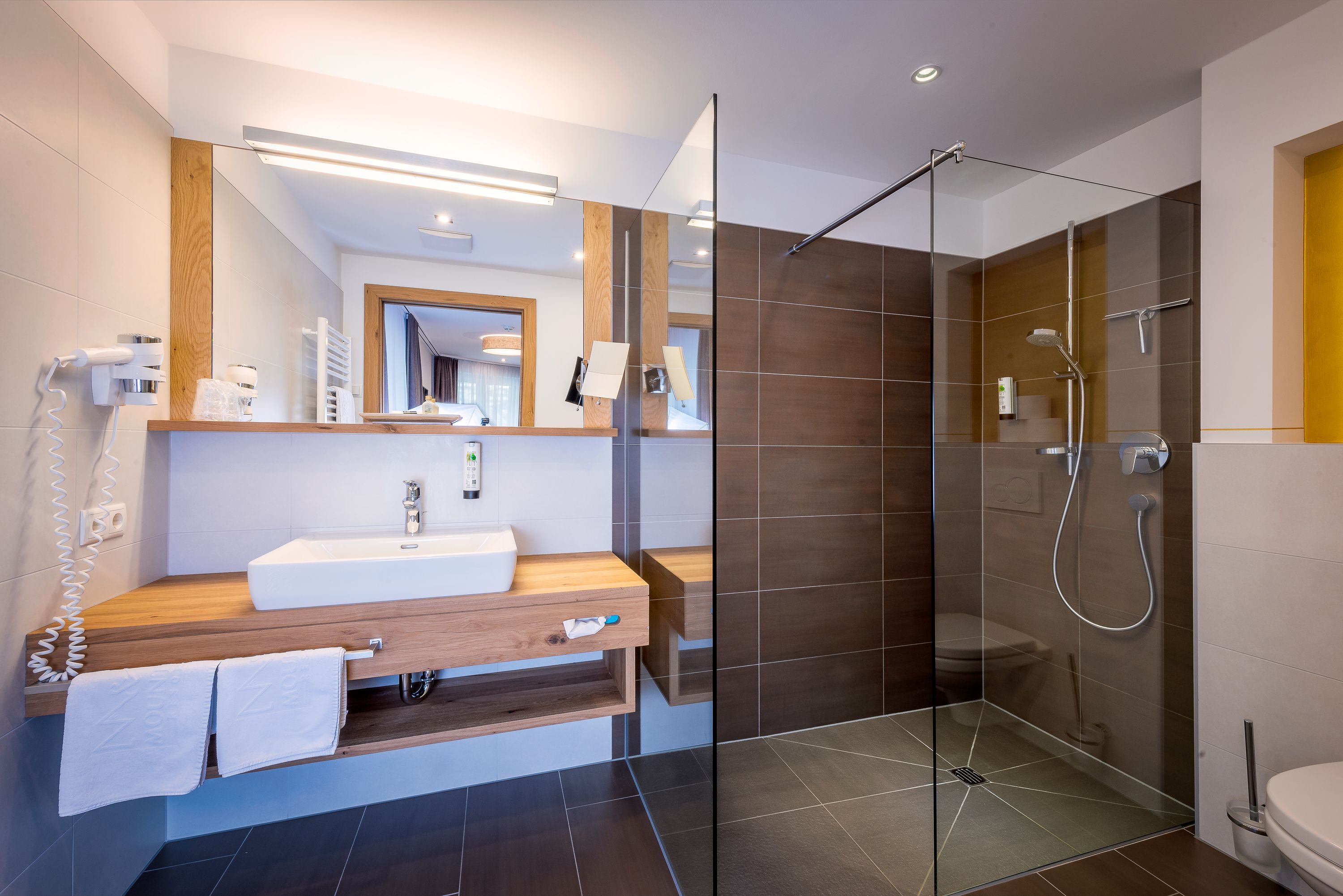 A modern bathroom with a wooden vanity, a glass shower enclosure, and a visible toilet.