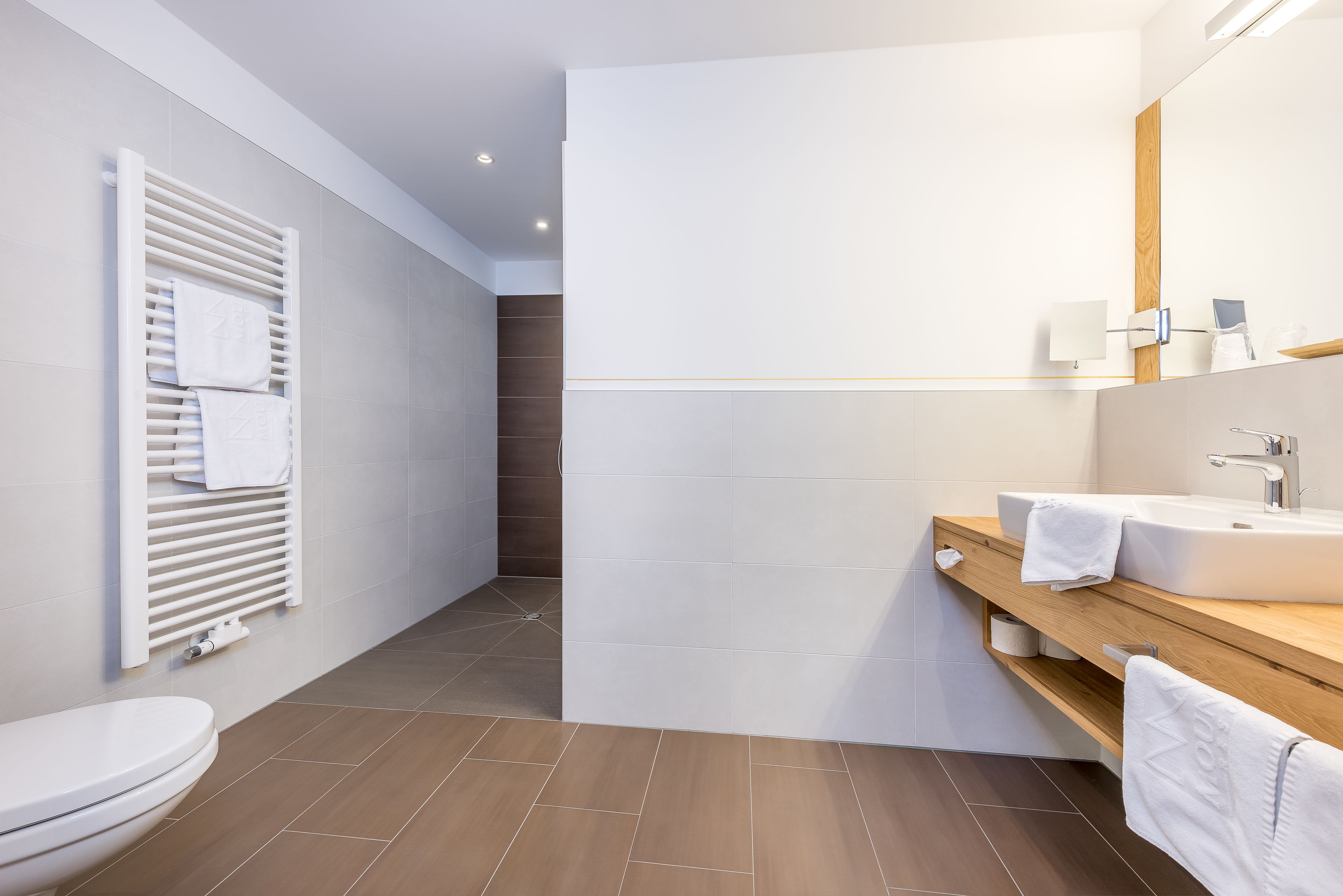 A modern bathroom with a toilet, a towel rack, a shower area, and a vanity with a mirror and sink.