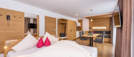 A modern hotel room with a large bed, wooden walls, a dining area, and a TV.