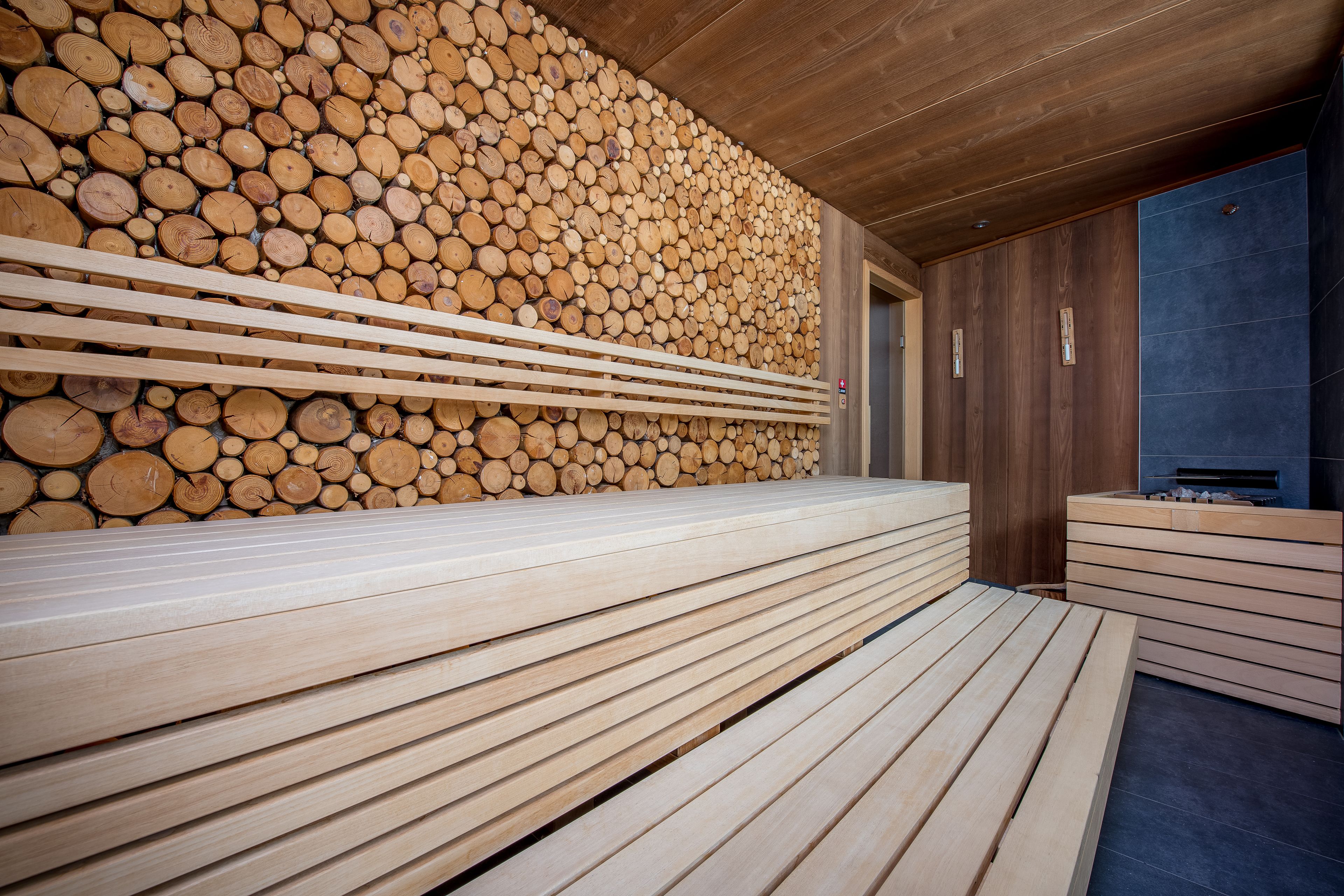 Una sauna con bancos de madera y una pared de leña apilada.