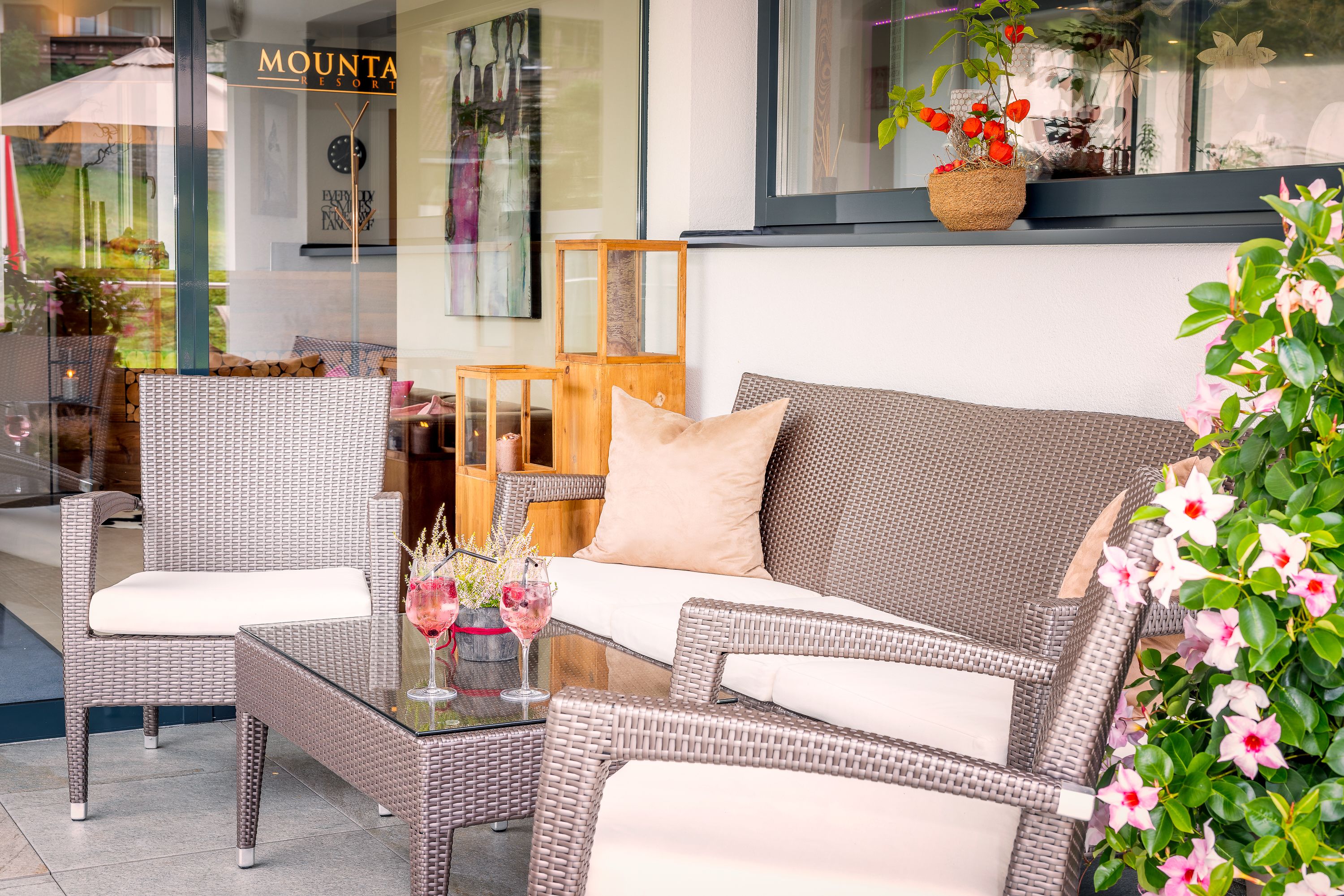 A wicker sofa with cushions, a glass coffee table, and a chair.