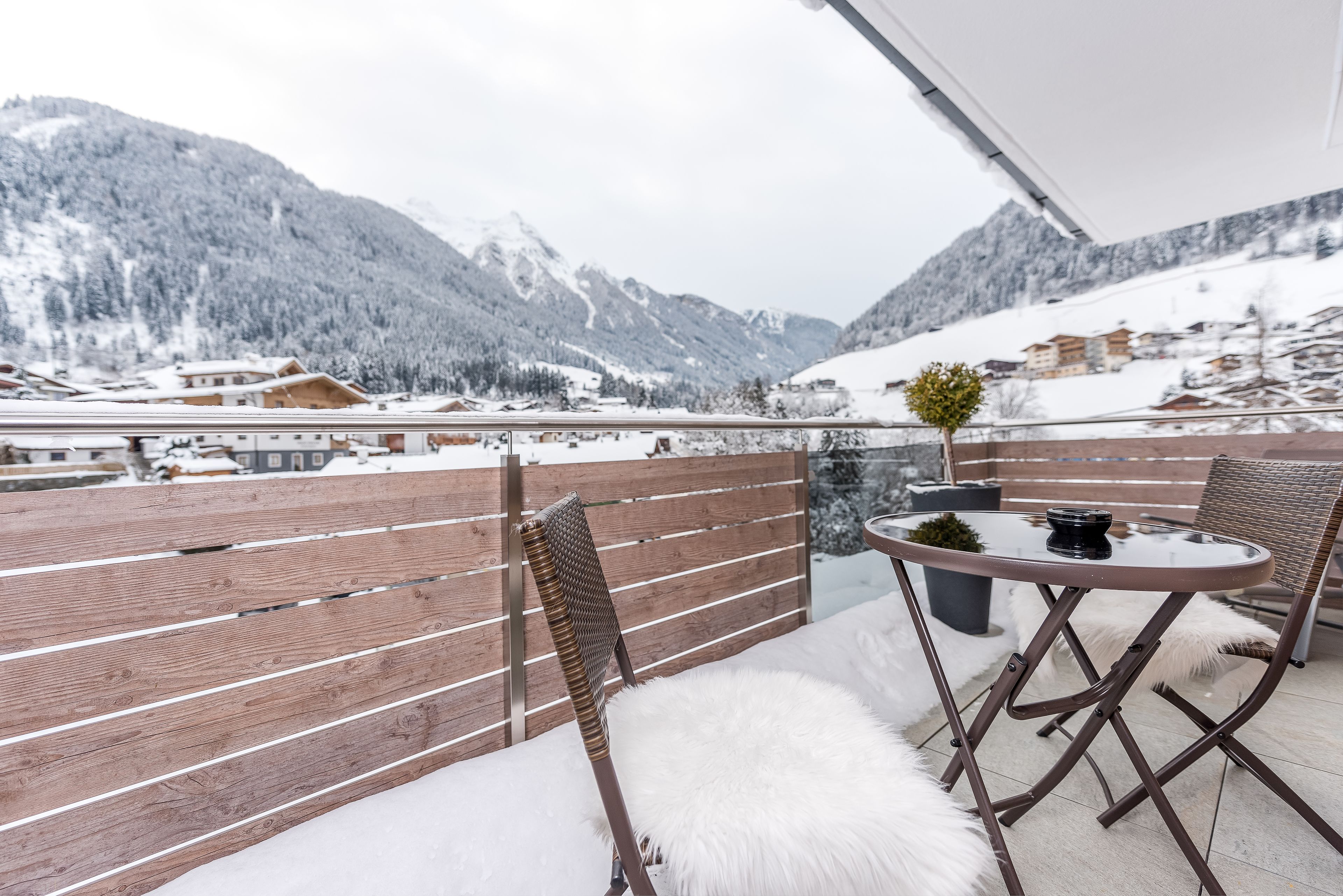 A balcony with a wooden railing, a round table, and two chairs.
