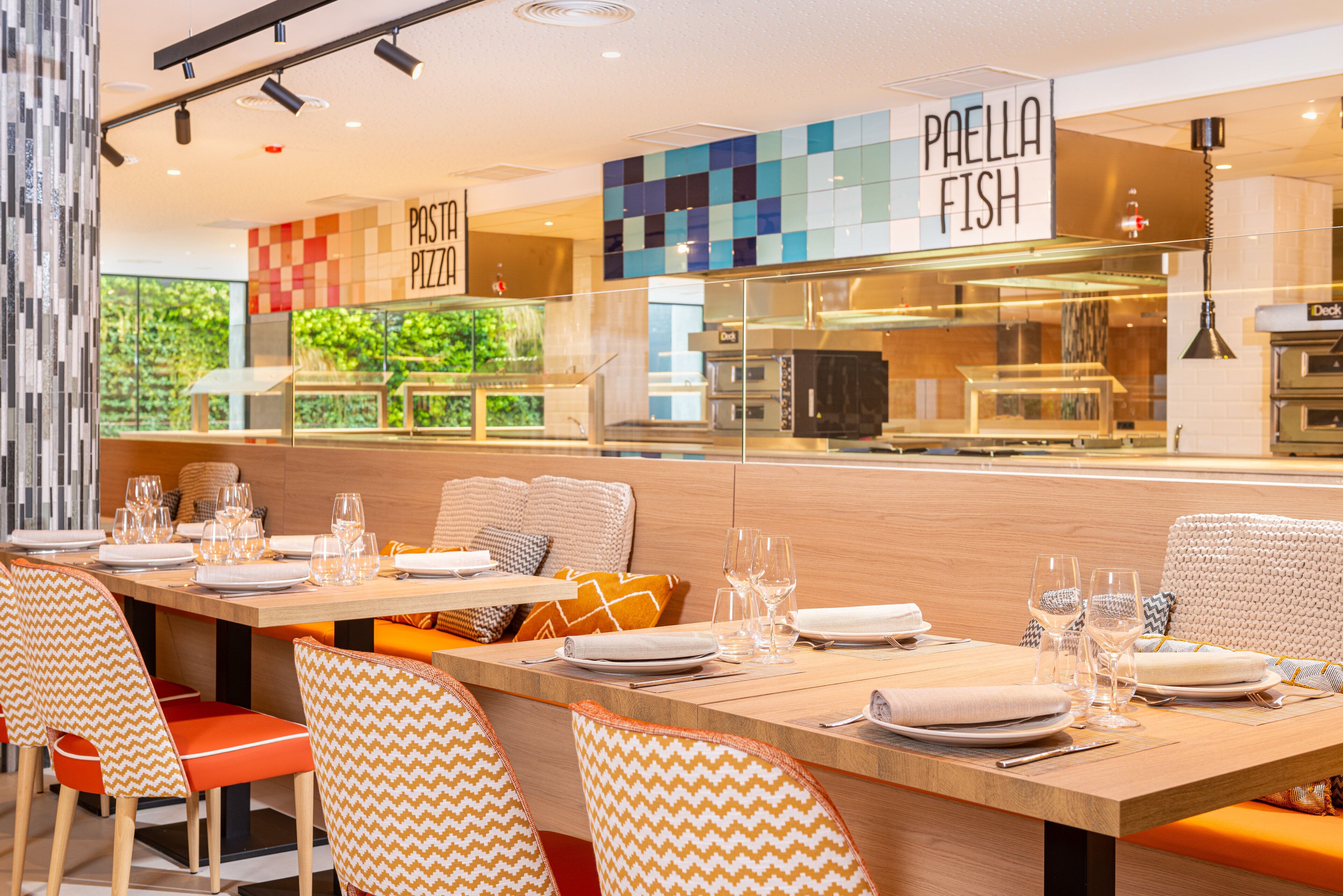 Un restaurante con una decoración moderna, que presenta una mesa de comedor de madera, sillas estampadas y vistas al área de la cocina.