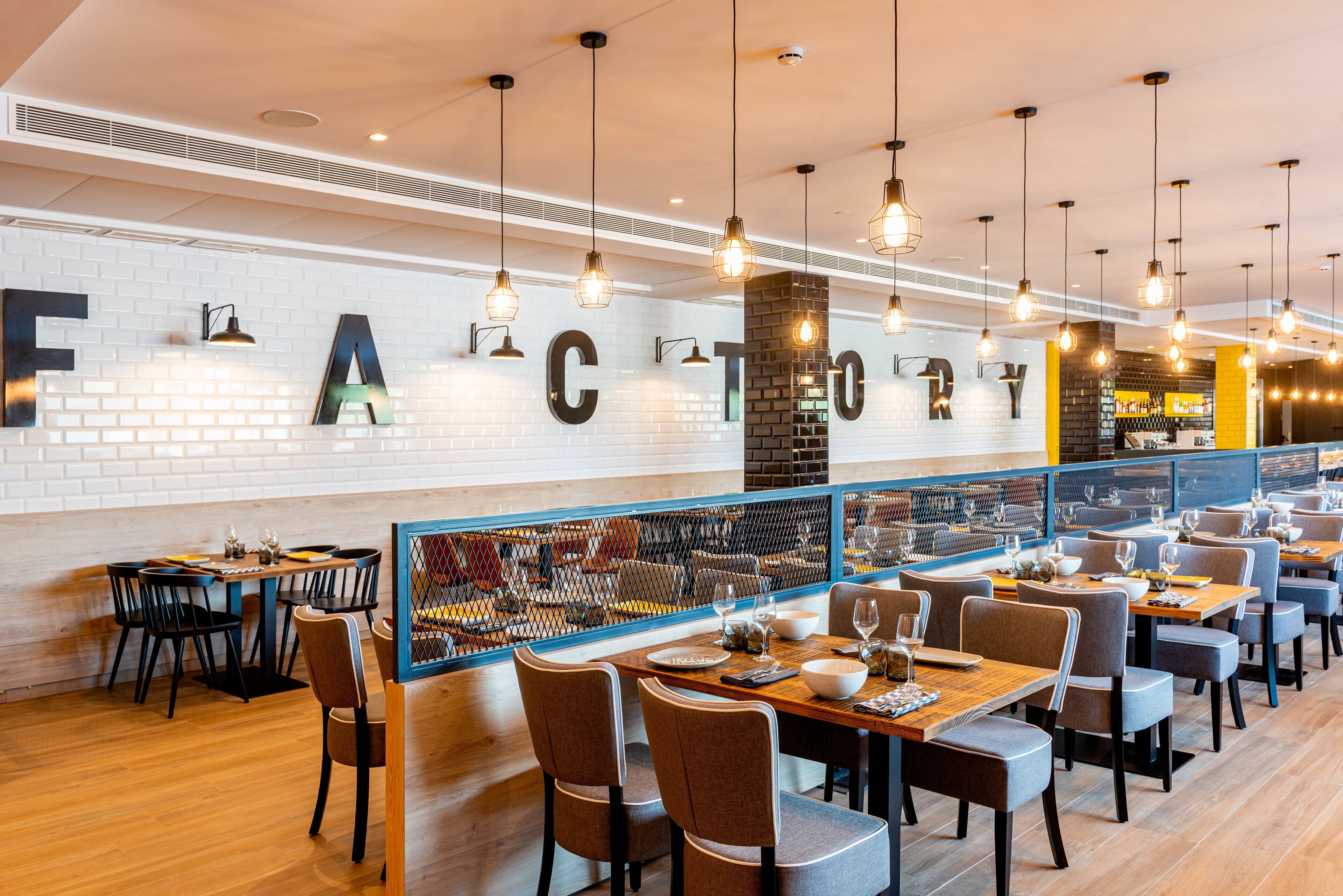 A modern restaurant with a brick wall and hanging light fixtures. Tables are set with chairs and dining ware.