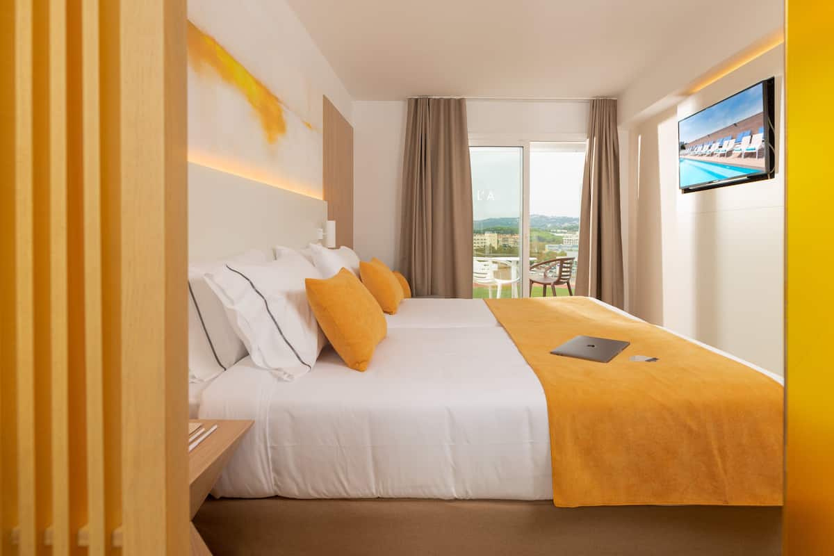 Une chambre d’hôtel avec un lit, un bureau, un ordinateur portable, une télévision et une vue sur la ville.