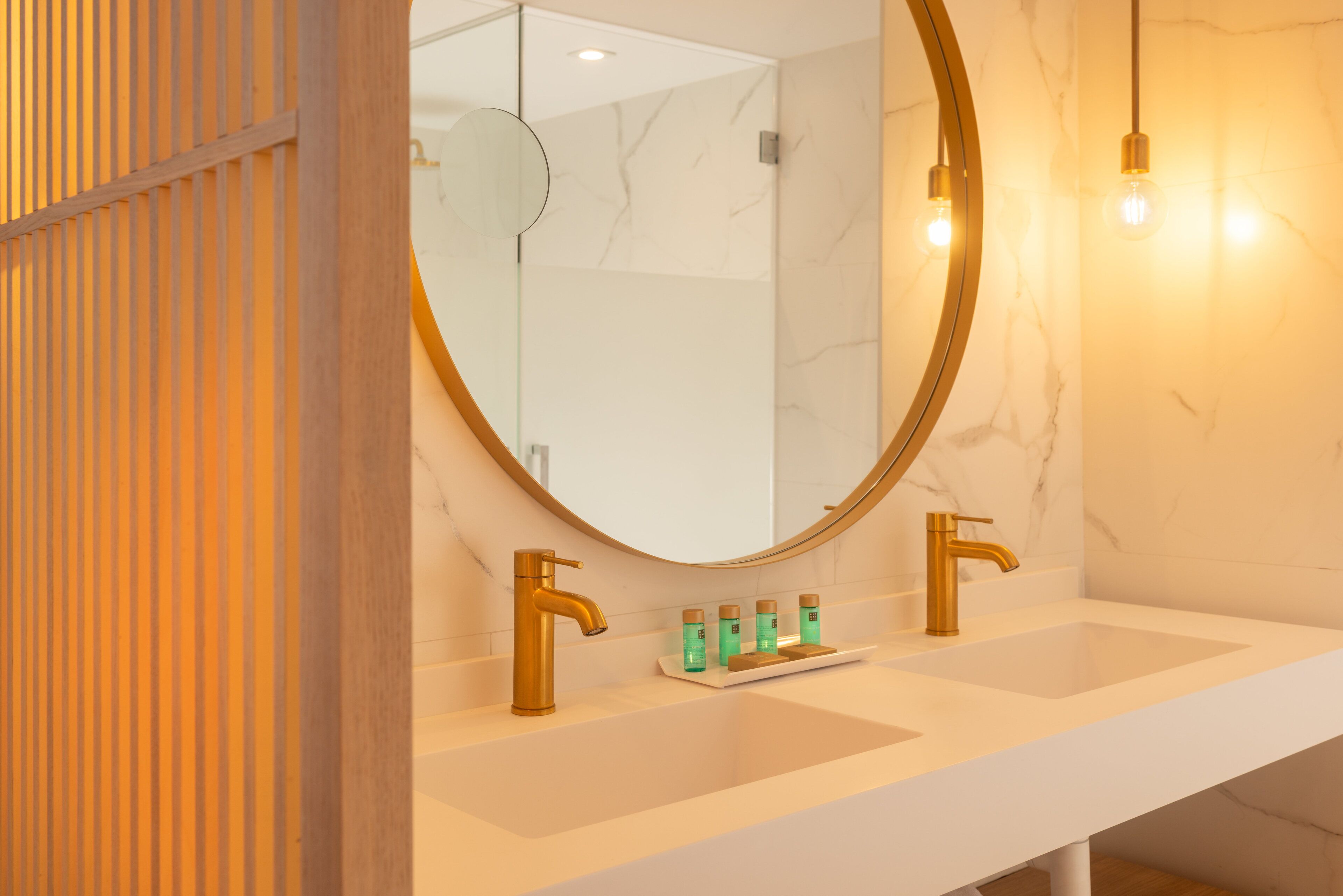 A bathroom with a white marble sink, gold faucets, and a round mirror.