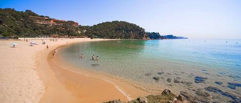 A beach with clear water, sandy shore, and rocky outcrops.