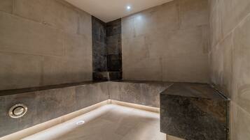 Un baño moderno con ducha en esquina, paredes con azulejos y un banco integrado.
