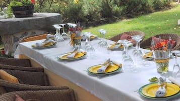 Zona d'esmorzar a l'aire lliure amb una taula llarga preparada per a un àpat, envoltada de cadires de vímet i coixins.