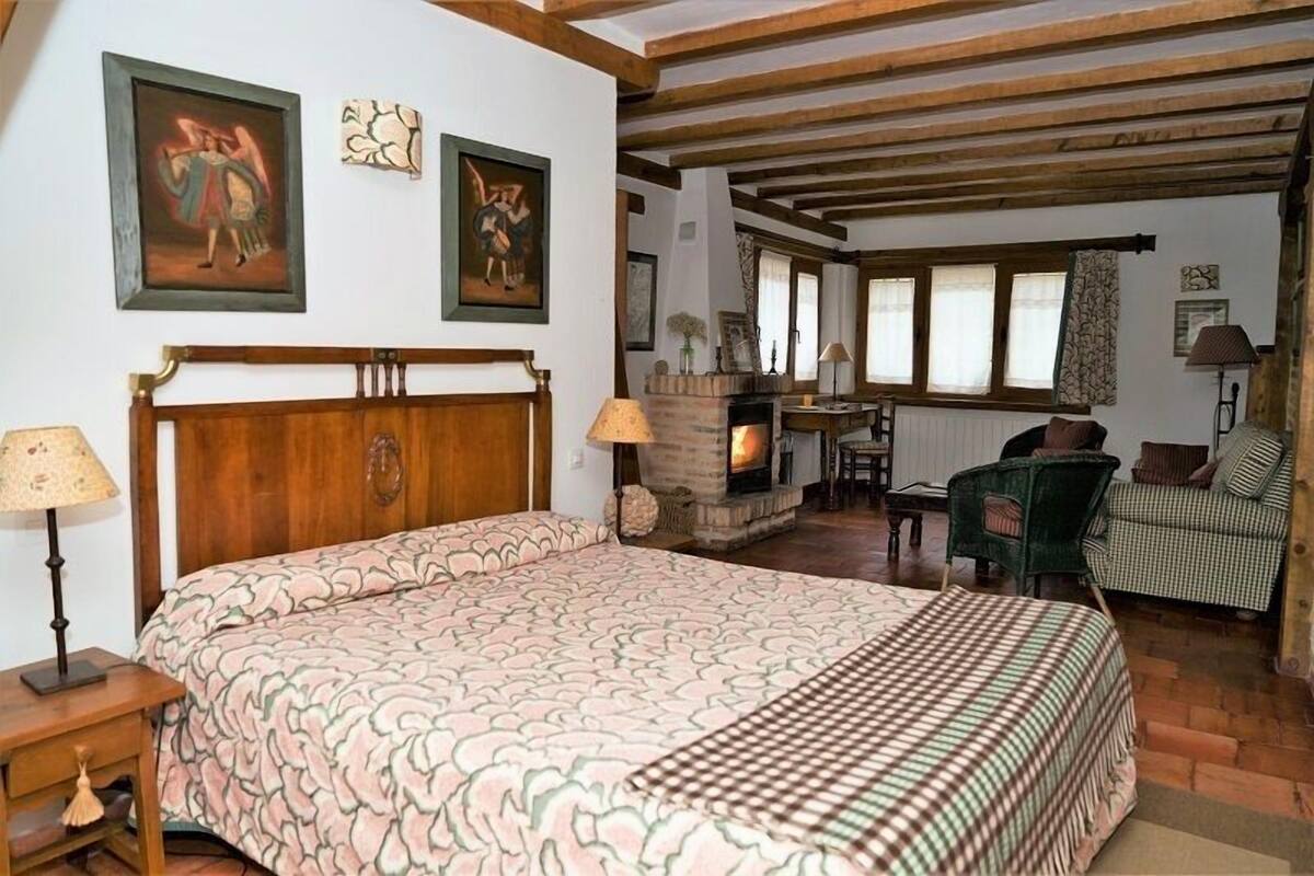 Une chambre avec un grand lit, des poutres en bois, une cheminée et une fenêtre avec des rideaux.