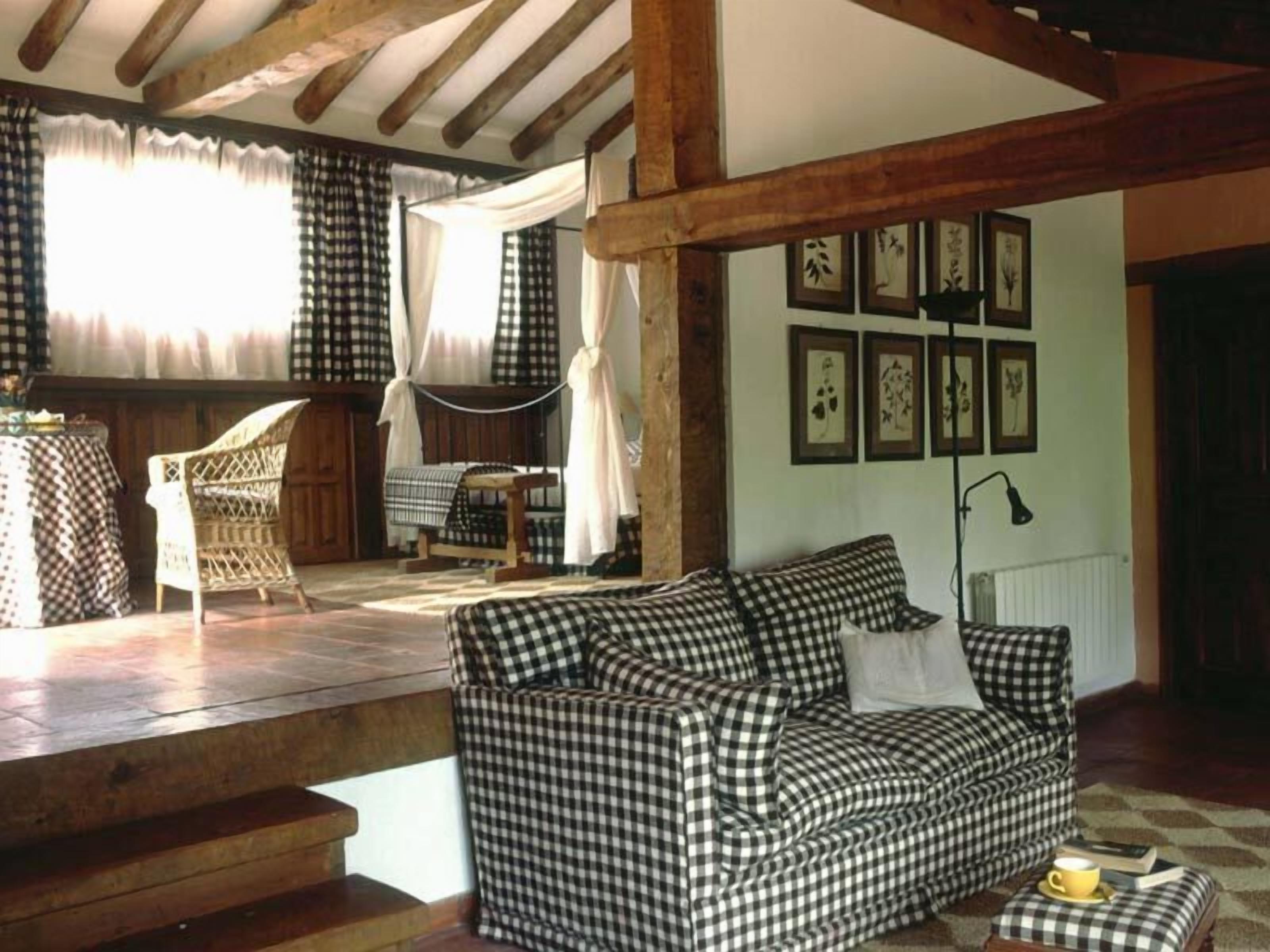 Un salón acogedor con un sofá a cuadros, una silla de mimbre y una mesita. Hay cuadros enmarcados en la pared y una lámpara sobre una mesita auxiliar.