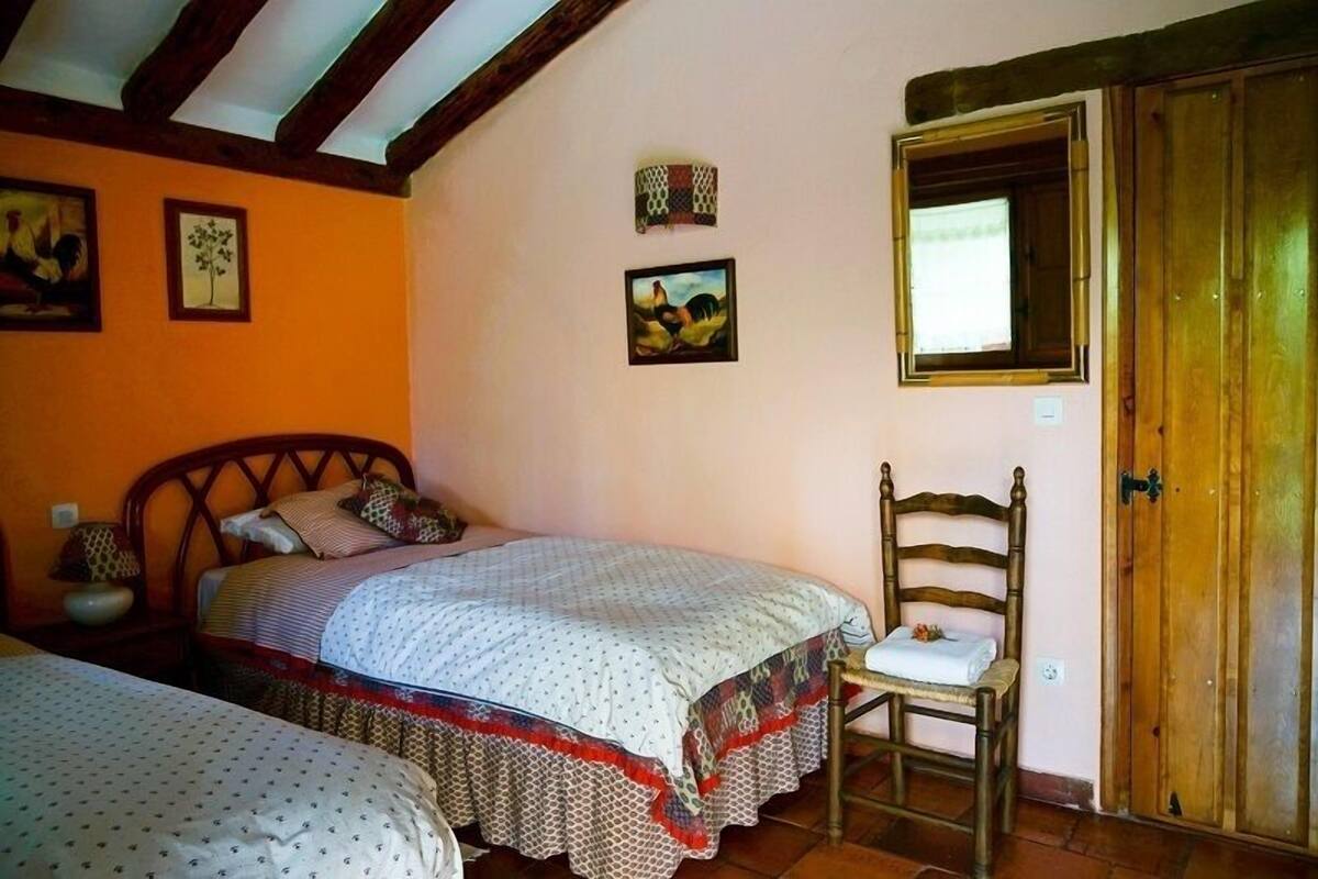 Une chambre avec deux lits, une chaise en bois, une armoire et deux tableaux accrochés au mur.