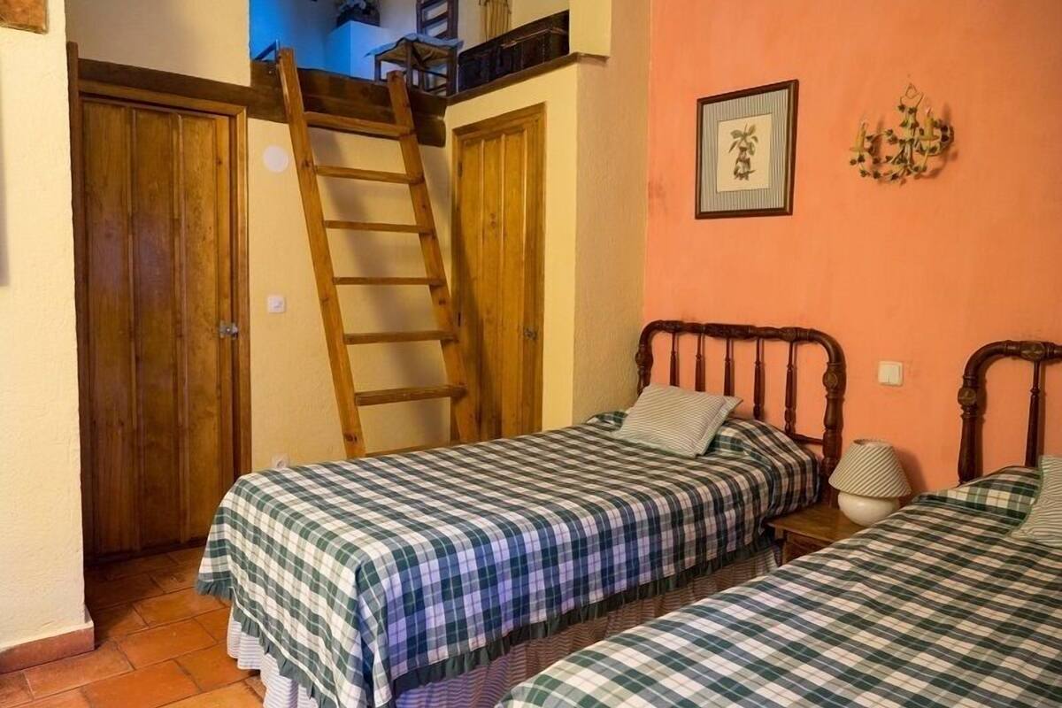 Une chambre avec deux lits, une échelle en bois et une armoire en bois.