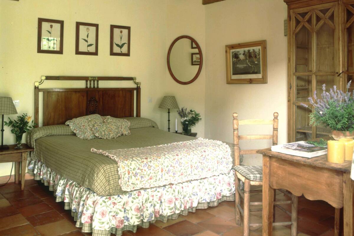 Une chambre à coucher avec un lit en bois, une chaise en bois, une armoire en bois et un miroir accroché au mur.