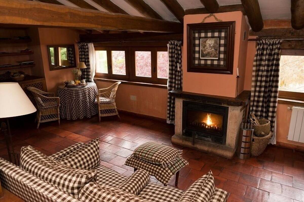 Un salon chaleureux, avec des meubles à motifs à carreaux, une cheminée et une vue dégagée sur l’extérieur grâce à de grandes fenêtres.