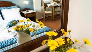 A hotel room with a bed, a nightstand, a table with a lamp, and a chair. There is a vase with yellow flowers on the nightstand and another vase with yellow flowers on the table.