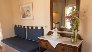 A room with a bed, a small table with a vase of flowers, a mirror, and a painting on the wall.