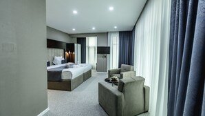 A modern hotel room with a large bed, a sofa, a flat-screen TV, and a minibar. - Parallel Hotel (Baku)