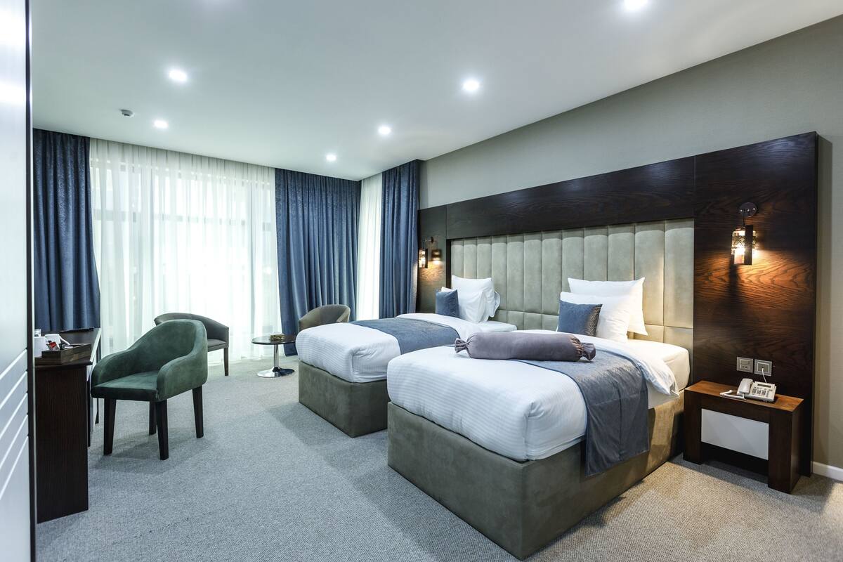 A modern hotel room with two beds, a desk, a chair, and a bedside table with a phone.