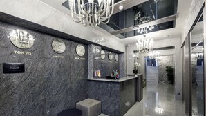 A modern lobby with a marble wall, clocks indicating different cities, a reception desk, and a chandelier. - Parallel Hotel (Baku)