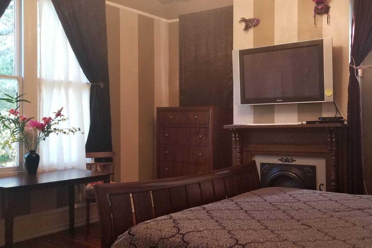 A bedroom with a bed, a television, a fireplace, a desk, and a window with curtains.