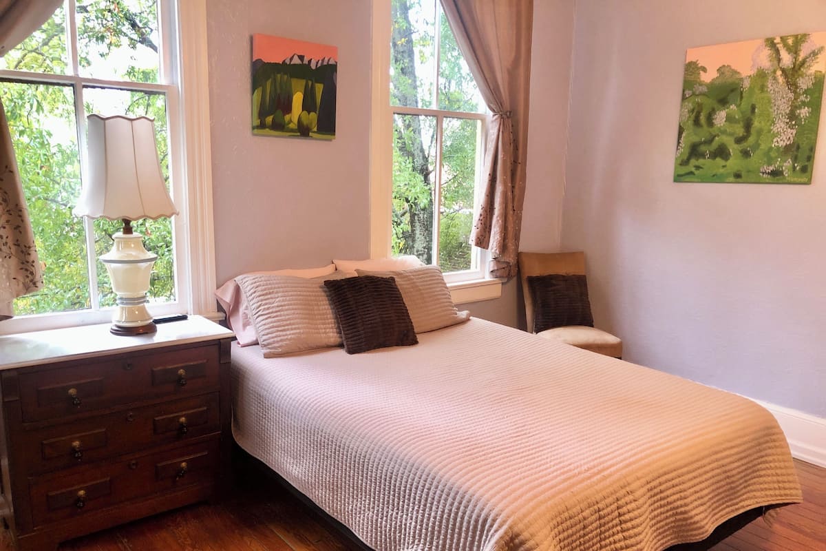 A bedroom with a bed, a dresser, a lamp, and two paintings on the walls.