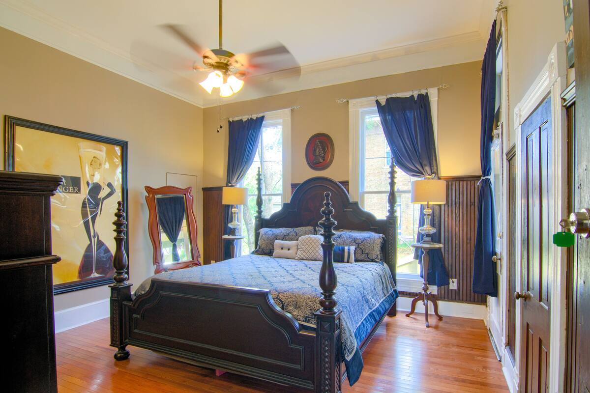 A bedroom with a large bed, a ceiling fan, and a window with curtains.