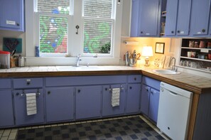 A kitchen with two sinks, a dishwasher, and cabinets with towels hanging. - The Mardi Gras House (Mobile)