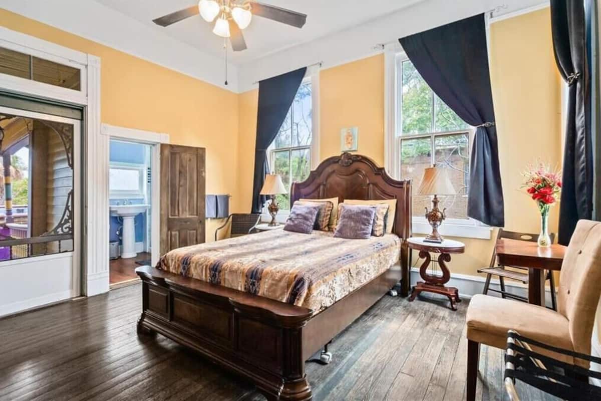 A bedroom with a wooden bed, two bedside tables with lamps, a chair, and a window with curtains.