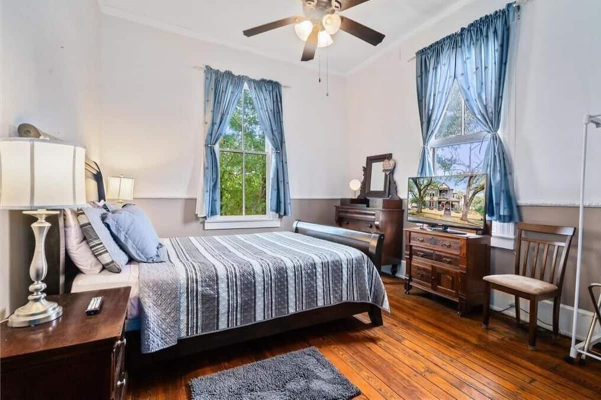 A bedroom with a bed, dresser, TV, and a ceiling fan.