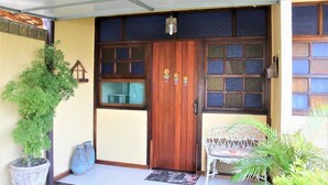 Una puerta de madera con paneles de vidrio, una planta en maceta y una silla blanca frente a un edificio.