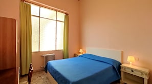A bedroom with a bed, two bedside tables with lamps, a radiator, and a window with curtains. - Hotel  Rita  Major (Florence)