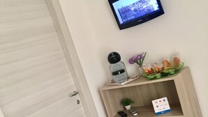 A hotel room with a wooden door, a television mounted on the wall, a small shelf with a remote control, a plant, and a card holder. - Casa Vacanze Da Angela (Sciacca)