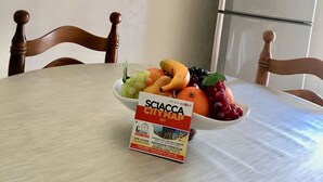 A dining table with a fruit bowl, a travel brochure, and a decorative item on the wall. - Casa Vacanze Da Angela (Sciacca)