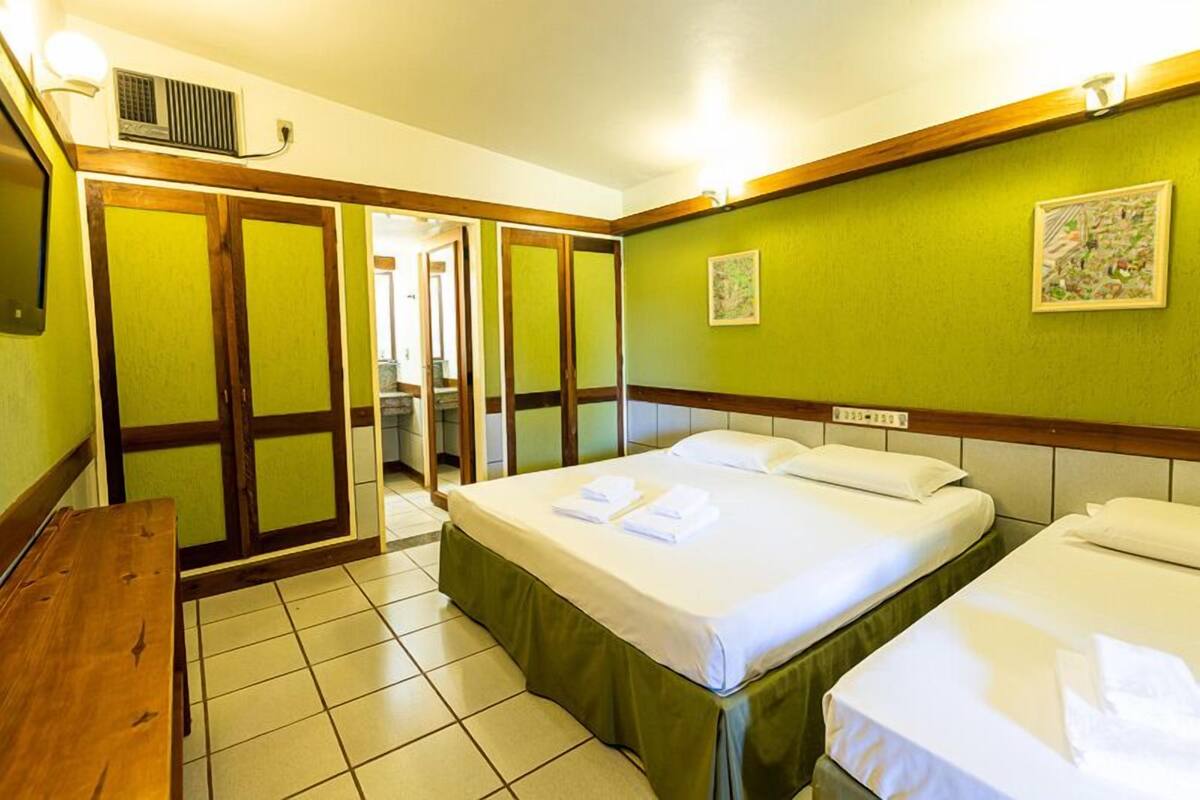 A hotel room with two beds, a wooden bench, and a green wall.