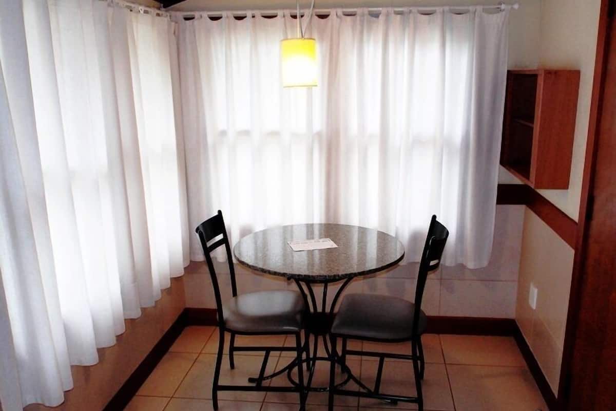 A dining area with a round table, four chairs, a hanging light fixture, and white curtains.