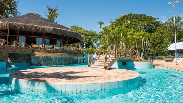 A pool area with a thatched-roof structure, a stone wall, and a water feature. - Hotel Estância Barra Bonita (Barra Bonita)