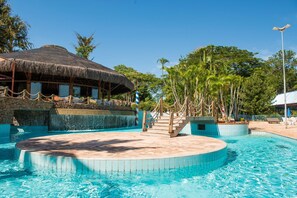 Un área de piscina con una estructura de techo de paja, pared de piedra y una fuente de agua.