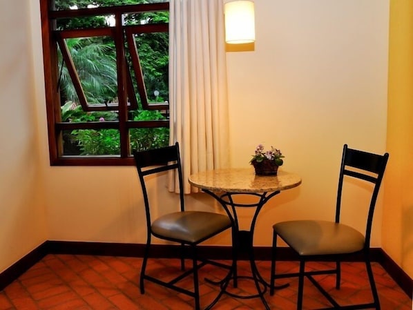 Una habitación pequeña con ventana, dos sillas, una mesa y una planta en maceta.