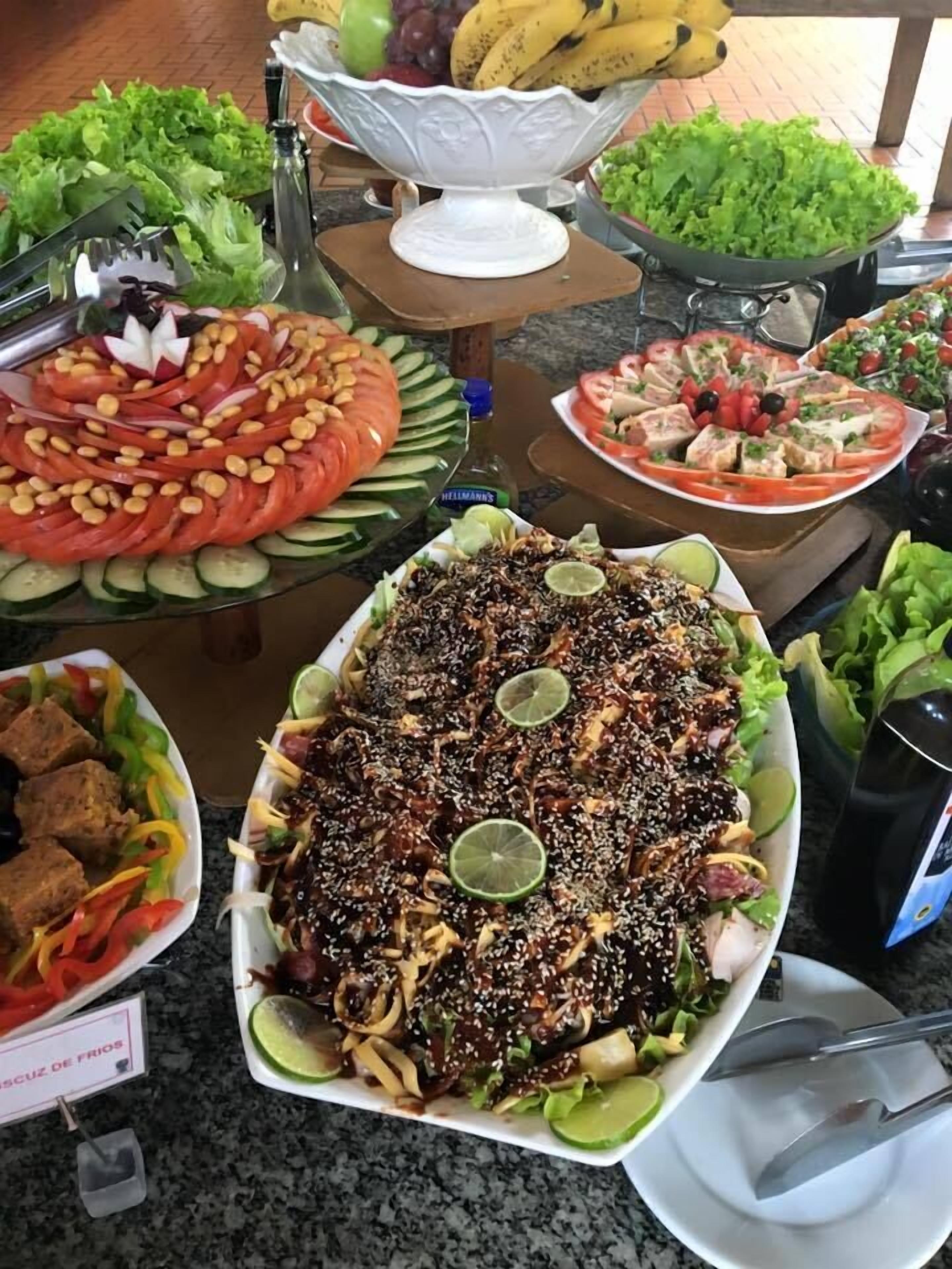 Buffet com diversos pratos, incluindo uma salada grande, vegetais fatiados e carne.