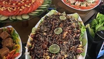 Buffet com diversos pratos, incluindo uma salada grande, vegetais fatiados e carne.