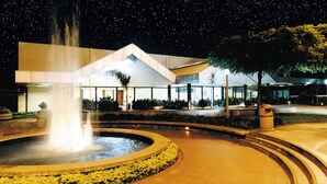 A nighttime view of a building with a central fountain, surrounded by a circular walkway and landscaped areas. - Hotel Estância Barra Bonita (Barra Bonita)