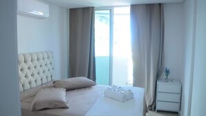 A hotel room with a large bed, a small bedside table, and a window with curtains. - Lindo Amplo 3 Quarto em Prédio Frente Mar (Cabo Frio)