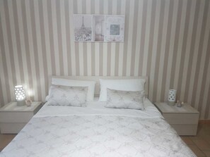 A neatly arranged bedroom with a striped wall, a bed with patterned bedding, two bedside tables with lamps, and a framed picture above the bed. - Iris B&b (Santa Maria la Carita)