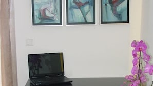 A workspace with a laptop on a desk, a chair, and three abstract paintings on the wall. - Harisis Apartments (Katerini)