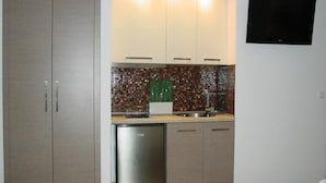 A compact kitchen with a refrigerator, a microwave, and a sink. There is a flat-screen TV mounted on the wall. - Harisis Apartments (Katerini)